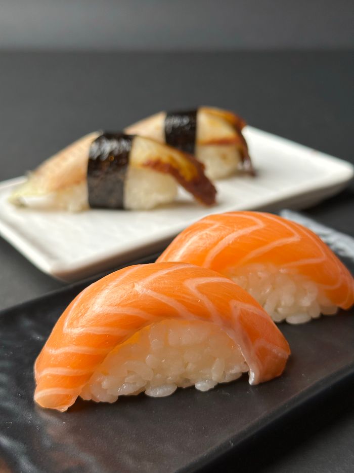 Close-up of fresh salmon and eel sushi nigiri with rice on black and white plates, showcasing Japanese cuisine.